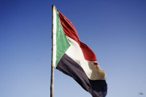 Sudanese flag waving on a pole against a clear blue sky.