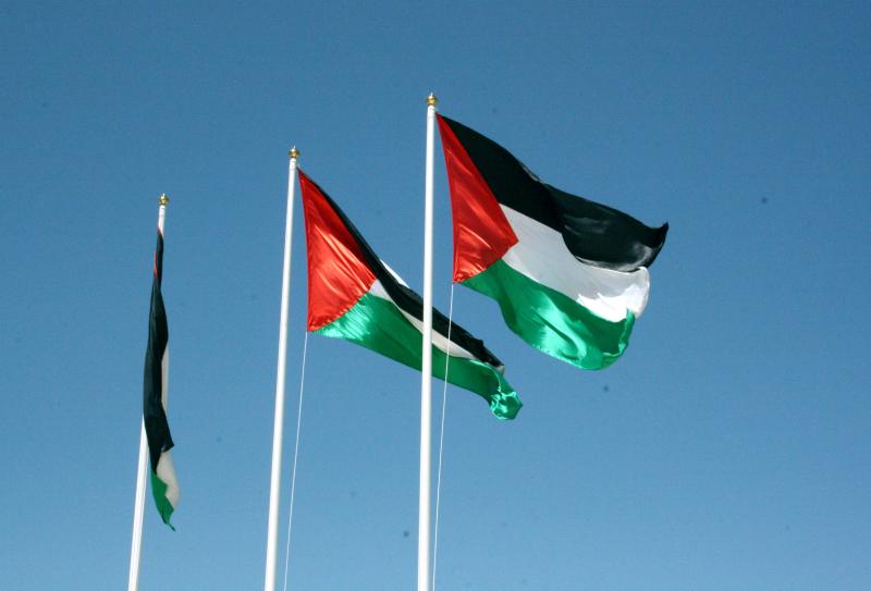 Three Palestinian flags waving on flagpoles against a clear blue sky.