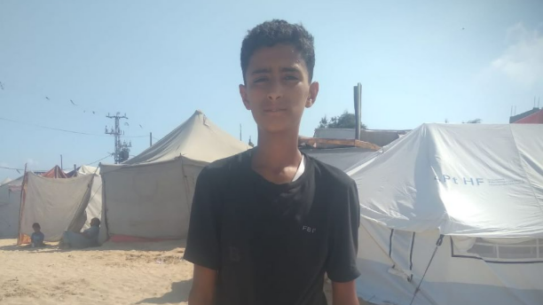 Hani, a 15-year-old orphan in Gaza, standing in front of tents where he lives with his grandmother after losing his parents in a bombing.
