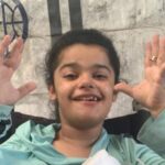 Save Rimas in Gaza – Rimas smiling and raising her hands while sitting in front of a tent.