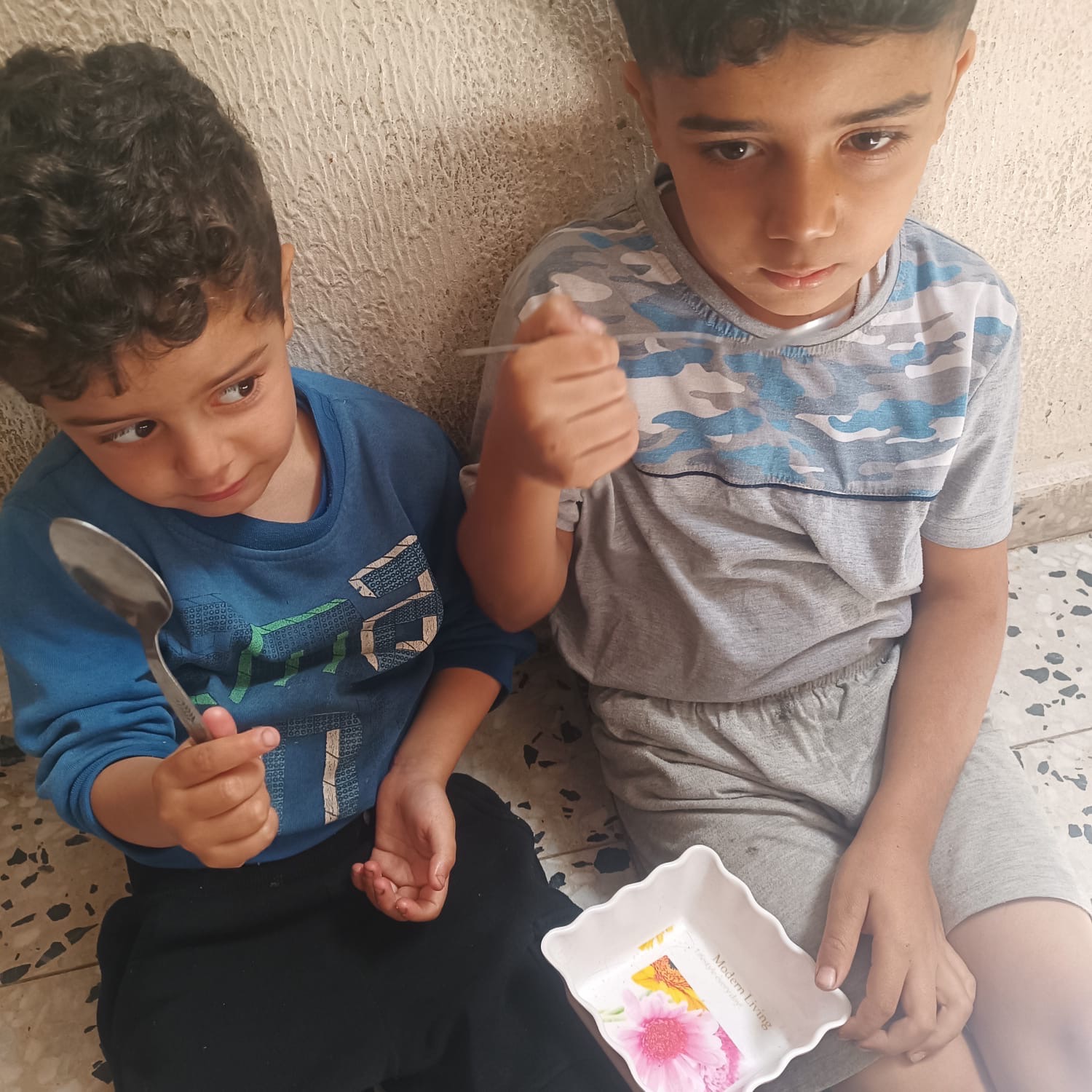 Two children holding spoons and an empty dish; image for Help Gaza family evacuate.