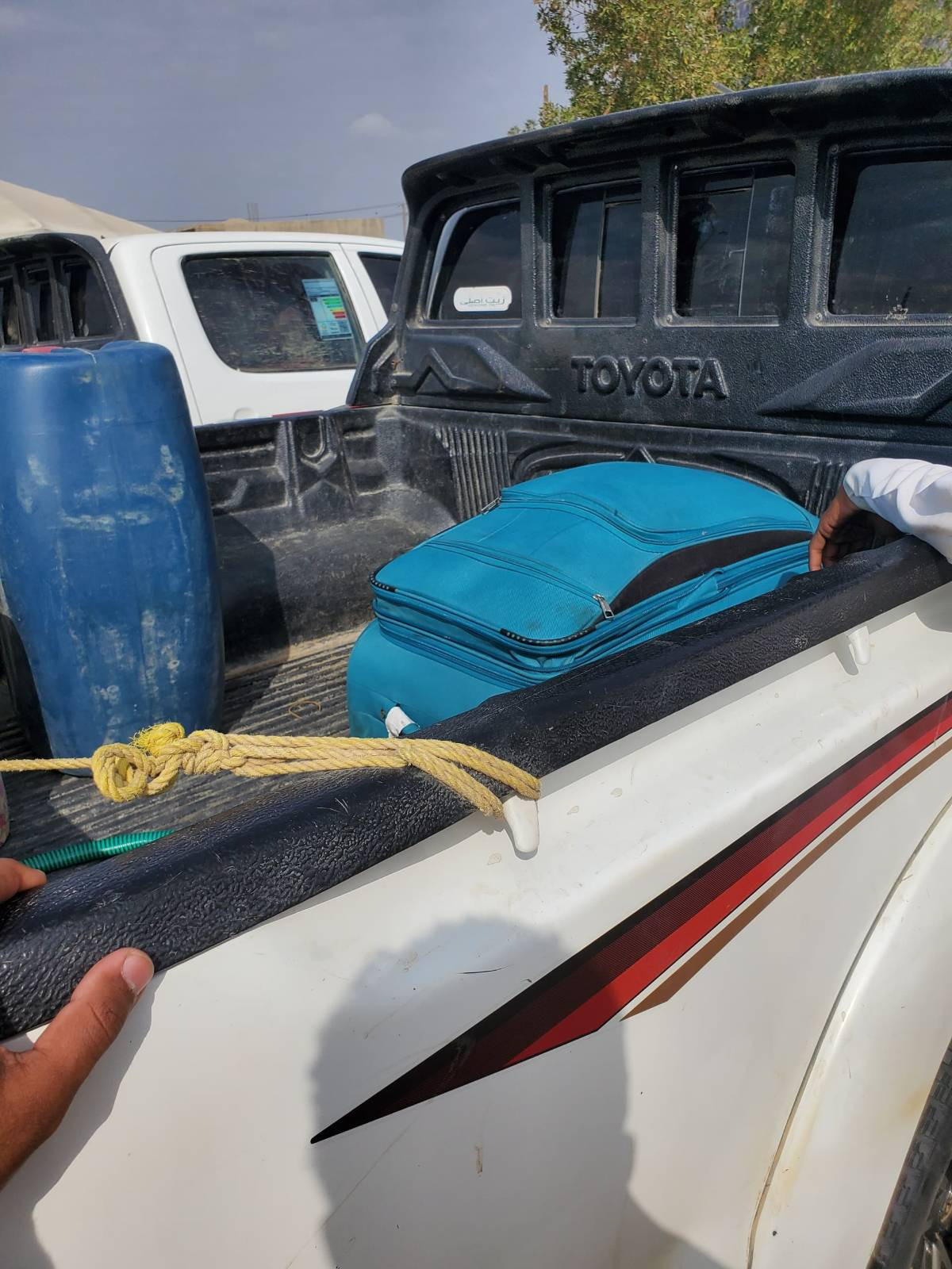 Sudanese student displaced with belongings packed in truck under tree, fleeing war.