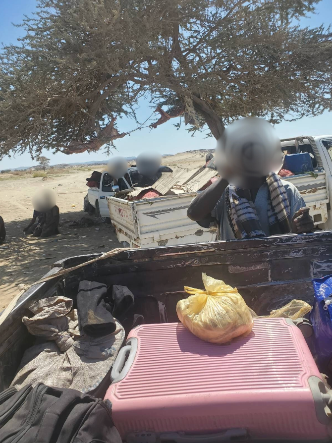 Sudanese student displaced with belongings packed in truck under tree, fleeing war.